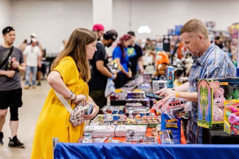 A shopper and vendor completing a purchase over a table of Hot Wheels and collectibles