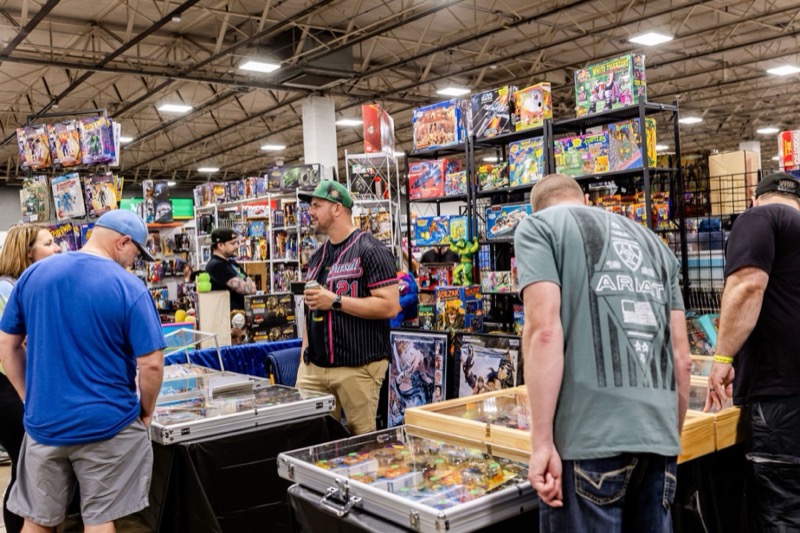 Attendees leaning over glass display cases while a vendor stands behind shelves of boxed toys