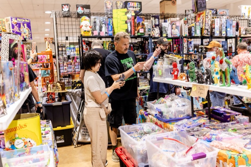 Fans talking over a Godzilla figure at a booth packed with kaiju and Ghostbusters toys
