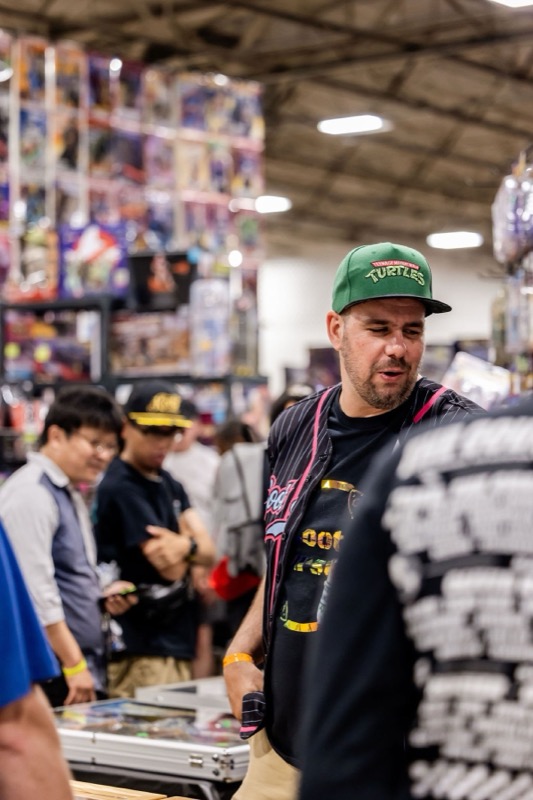 A collector in a Turtles hat browsing a towering wall of carded action figures