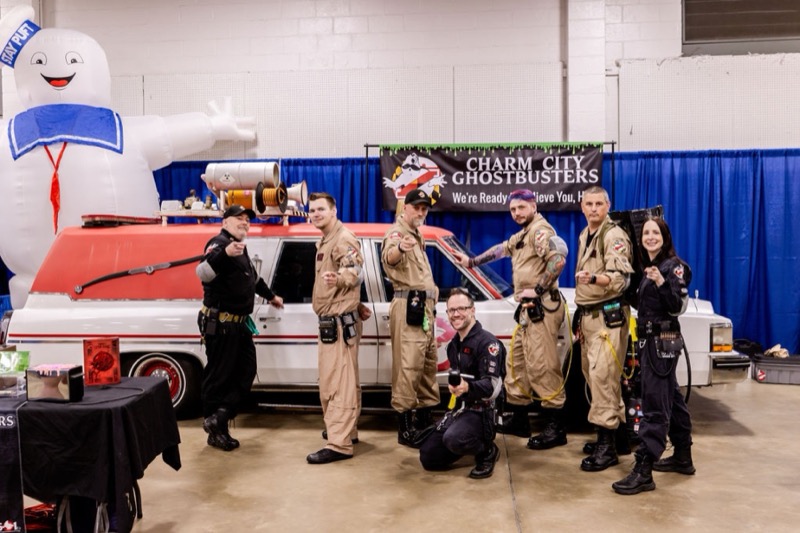 Charm City Ghostbusters cosplayers posing with an Ecto-1 replica and Stay Puft inflatable