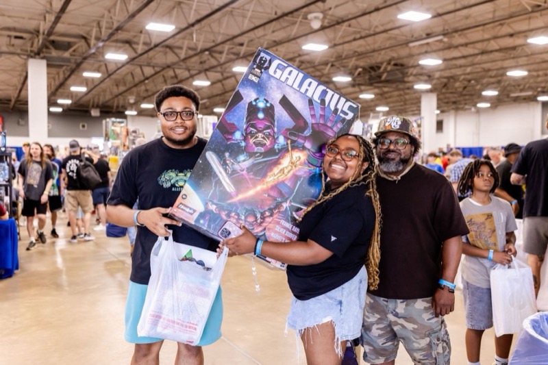 Three smiling attendees posing with a large HasLab Galactus box they found at the show