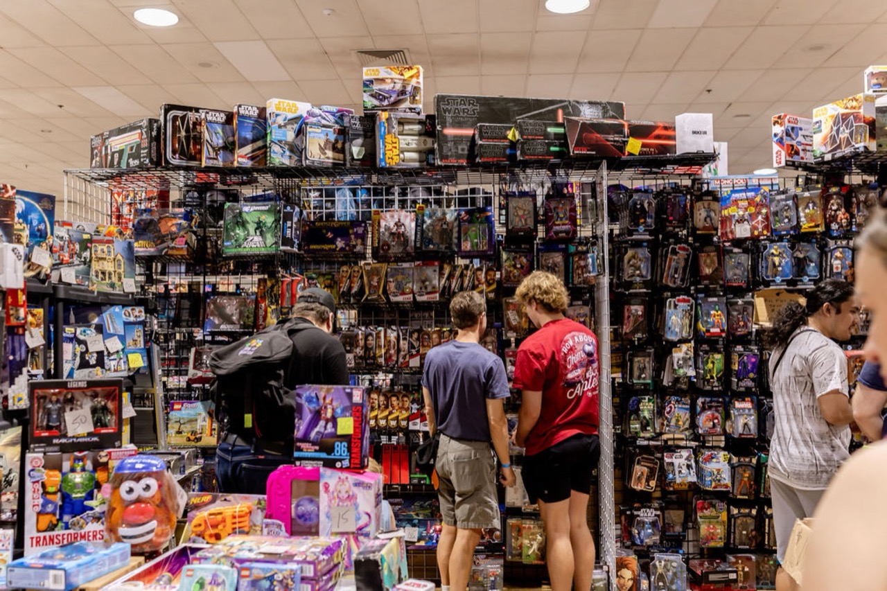 Collectors browsing a wall packed with Star Wars, Marvel, Transformers, and action figures at Maryland Toy Expo