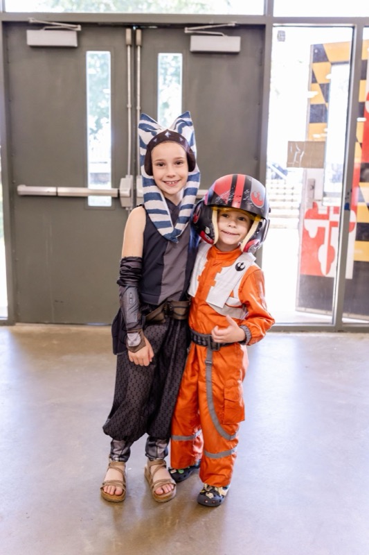 Two kids dressed as Ahsoka Tano and a Rebel X-wing pilot smiling and giving a thumbs up