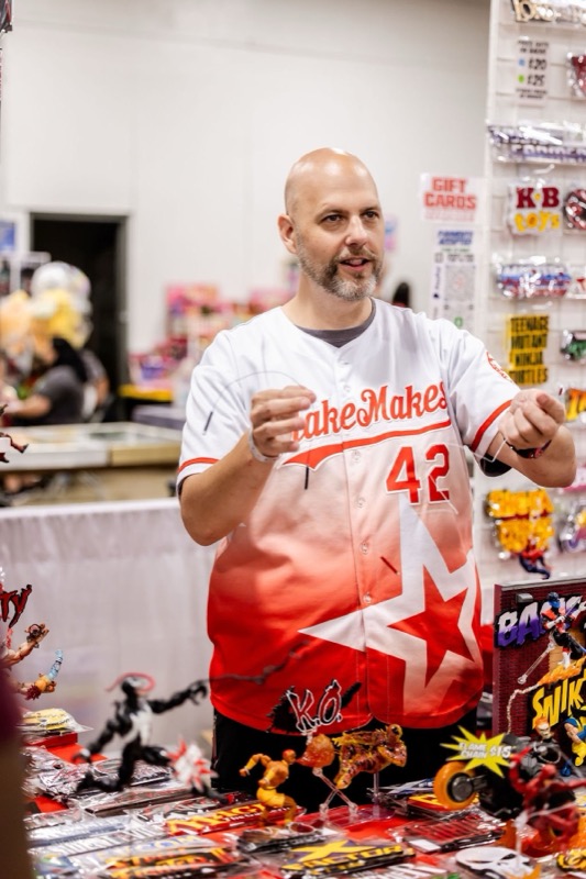 A vendor in a Fake Makes jersey behind a table of custom action figures